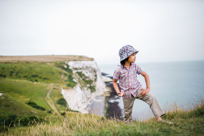 Boy standing on cliff against sky