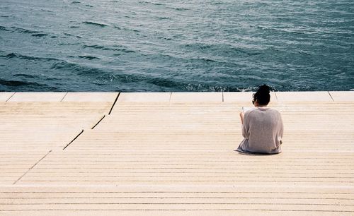 Rear view of woman sitting on steps against river during sunny day