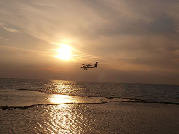 Silhouette person flying over sea against sky during sunset