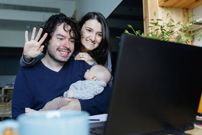 Happy father and mother with baby boy talking on video call through laptop