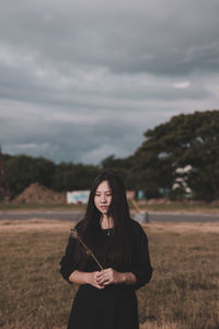 Portrait of young woman standing on field against sky