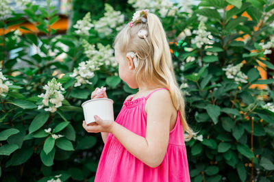 Young woman drinking water while standing against plants