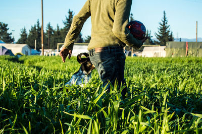 Midsection of man carrying ball with dog on field