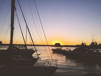 Silhouette sailboats moored in sea against sky during sunset