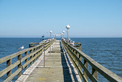 Pier over sea against clear blue sky