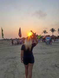 Rear view of woman photographing on beach during sunset