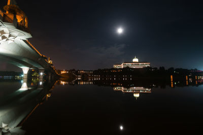 Illuminated city by river against sky at night