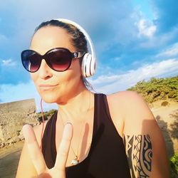 Happy woman listening music in headphones while showing peace sign against sky