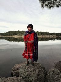 Man standing on rock looking at lake against sky