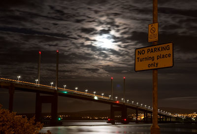 Illuminated road sign in city against sky at night