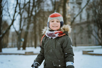 Winter portrait of cute caucasian 7 years old boy in knit hat with pompom in city