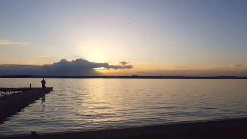 Silhouette man on sea against sky during sunset