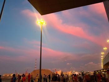 Low angle view of people on street against sky during sunset
