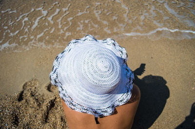 High angle view of woman wearing sun hat while sitting at beach on sunny day