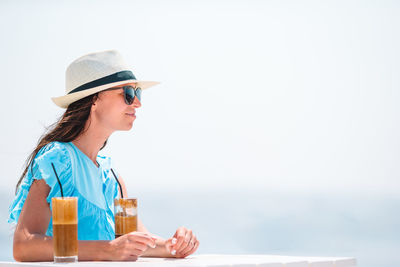 Side view of young woman drinking glass against water