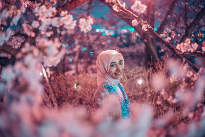 Portrait of young woman standing by cherry blossom tree