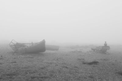 Abandoned boat on field against sky during foggy weather