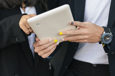 Businessman with painted nail using tablet pc with colleague