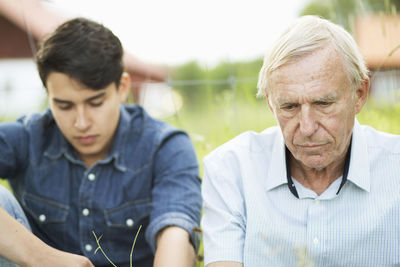 Thoughtful senior man with grandson sitting in yard