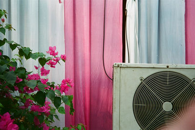 Air conditioner by fresh pink flowers against curtain