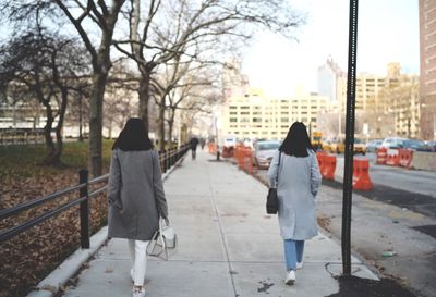 Rear view of women wearing coat walking on sidewalk in city during winter