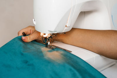 A woman sews turquoise fabric on a sewing machine. close-up of hands