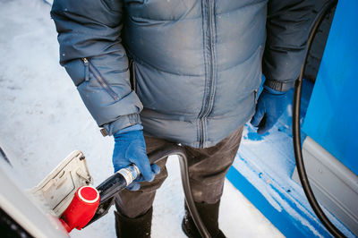 Low section of man refueling car with fuel pump during winter