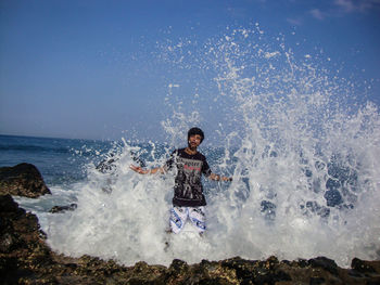 Full length of boy splashing water in sea against sky