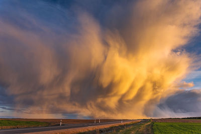 Scenic view of road amidst field against dramatic sky