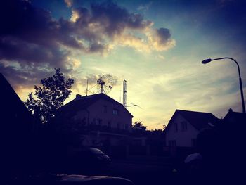 Street amidst silhouette buildings against sky at sunset