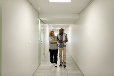 Full length of female nurse walking with senior man in corridor at retirement home