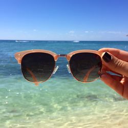 Cropped hand of woman holding sunglasses at beach against sky