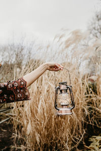 Midsection of woman holding plant on field against sky