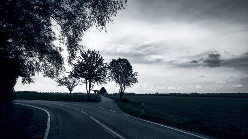 Road by trees on field against sky