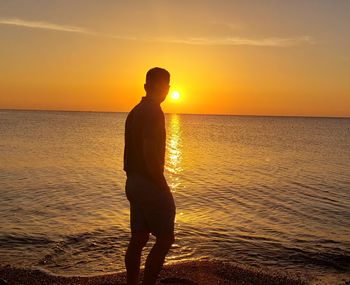 Silhouette man standing on beach against sky during sunset