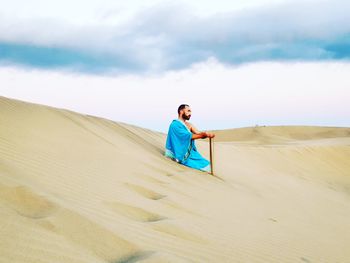 Man on sand dune in desert against sky