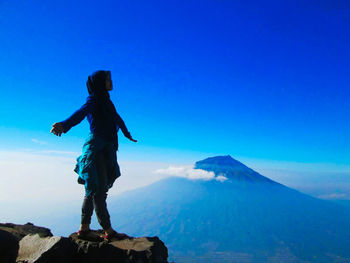 Side view of woman standing on mountain against blue sky