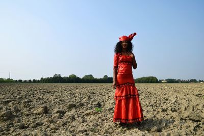Portrait of woman wearing red dress standing against sky