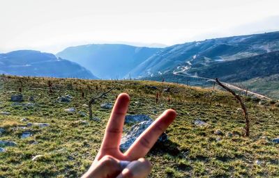 Cropped hand gesturing peace sign against mountains