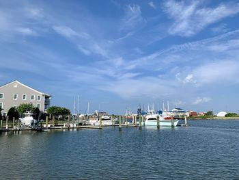 Sailboats moored in harbor by houses against sky