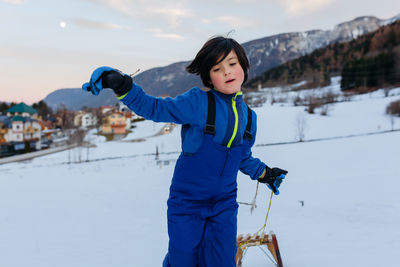 Girl with short dark hair pulling up the wooden sled in snowy mountain