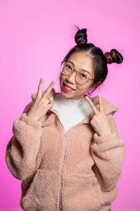 Portrait of smiling woman showing peace signs against pink background