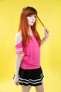 Young woman standing against yellow background