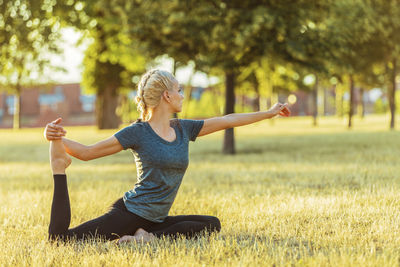 Full length of woman exercising yoga on grassy field at park