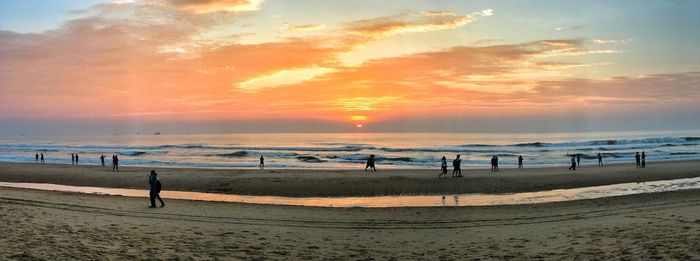 People standing on beach against sky during sunset