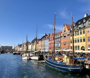 Sailboats moored on canal by buildings against blue sky