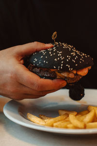 Male hand holding a beef burger with a black bun in a cafe. american delicious lunch