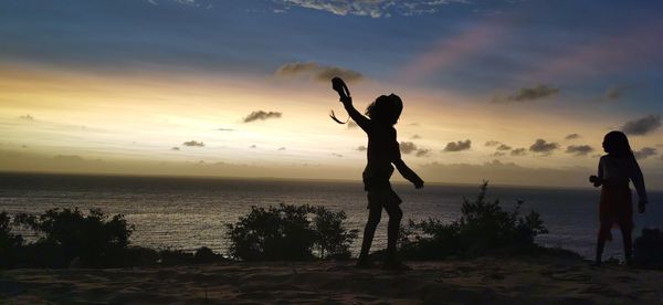 Silhouette woman standing on beach against sky during sunset