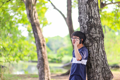 Side view of man wearing sunglasses on tree trunk