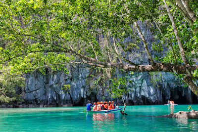 People on boat in water against trees